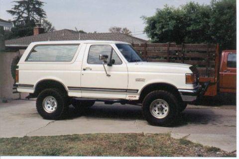 1990 Ford Bronco - A white Ford Bronco is parked on a concrete driveway next to a wooden fence.