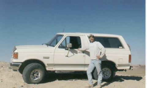 1990 Ford Bronco - White Ford Bronco with hardtop parked on open desert hardpack under a clear blue sky, shown from the driver's side with the door open. A pe…