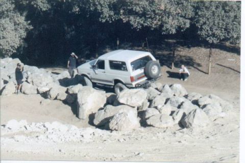 1990 Ford Bronco - A white 1990 Ford Bronco navigates a challenging rocky obstacle during an off-road trip.