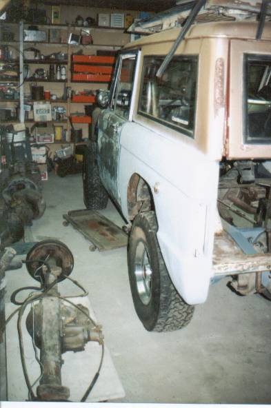 1966 Ford Bronco - A Ford Bronco is undergoing restoration in a cluttered garage, with various automotive parts visible.