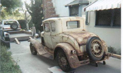 1966 Ford Bronco - Three-quarter rear view of a weathered 1930s Ford Model A coupe project in cream and rust patina, sitting on a trailer in a driveway with a…