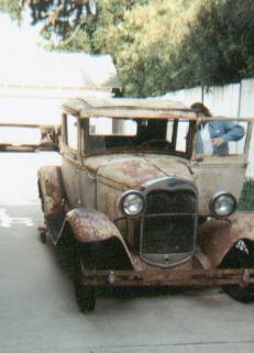1966 Ford Bronco - Three-quarter front view of a heavily rusted 1930s Ford Model A pickup project sitting on a paved driveway, with a bare radiator shell, exp…