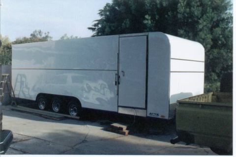 1990 Ford Bronco - White enclosed trailer with three axles parked on concrete, with trees in the background.