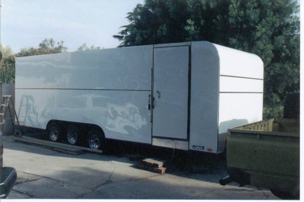 White enclosed trailer with three axles parked on concrete