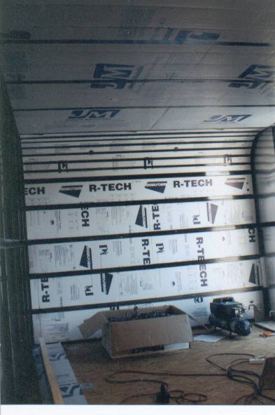 1990 Ford Bronco - The interior of a trailer or cargo space shows insulation being installed, with a box and engine on the floor.