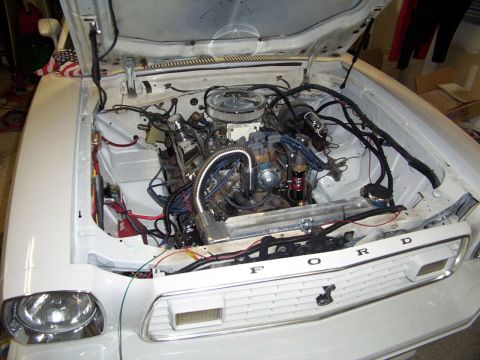 1978 Ford Mustang II - The engine bay of a white Ford Mustang II is open, revealing its V8 engine and front grille.
