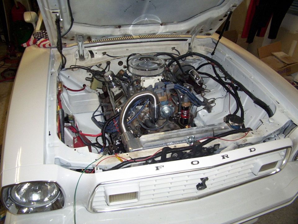White Ford Mustang II with hood open, showing the V8 engine and front grille with 'FORD' lettering