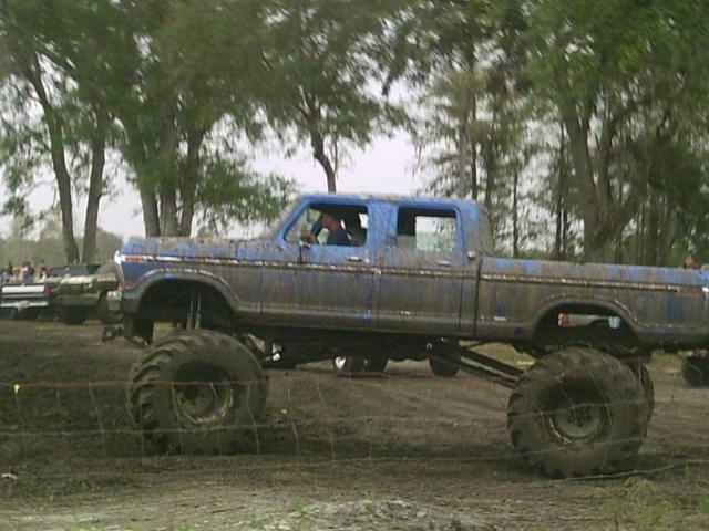 Blue lifted pickup truck with large tires in mud