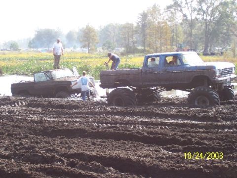 1993 Ford Bronco - Two trucks are stuck in a muddy field with people attempting to free them.