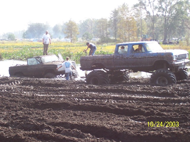 Two mud-covered trucks stuck in a muddy field with people around them