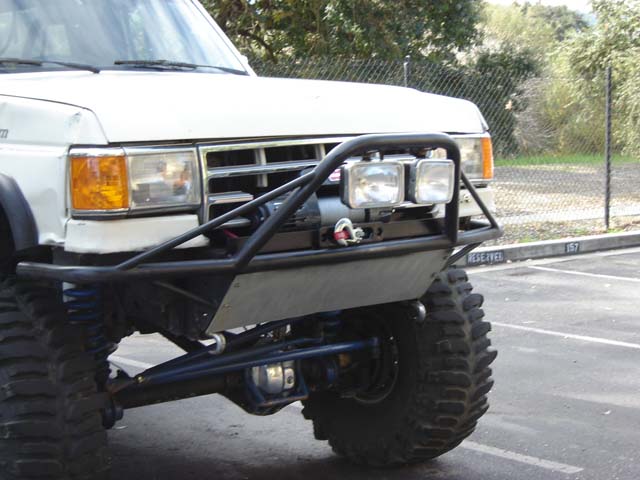 Front of lifted white SUV with tube bumper, winch, off-road lights and blue suspension