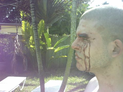 1992 Ford Bronco - A man with blood on his face is seen in profile outdoors near palm trees and lounge chairs.