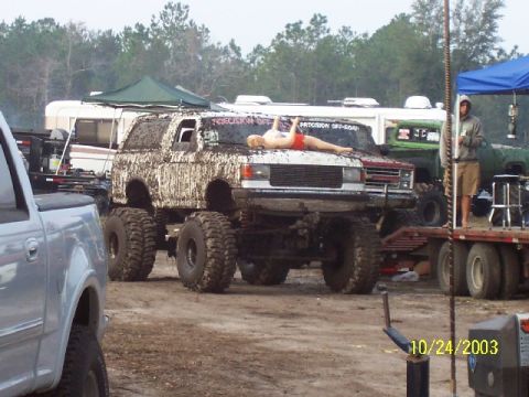 1995 Ford Bronco - Muddy lifted SUV with a person on the hood at an outdoor event. Multiple vehicles and RVs are visible.