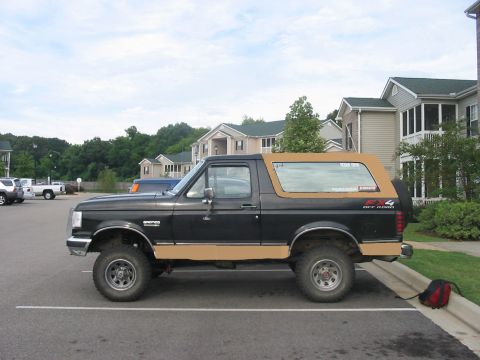1988 Ford Bronco - Side view of a black Ford Bronco with tan two-tone trim and a tan removable top.