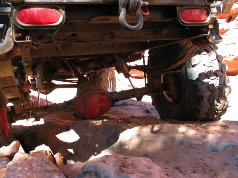 1987 Ford Bronco - Undercarriage view of an off-road vehicle's rear axle and suspension system on rough terrain.