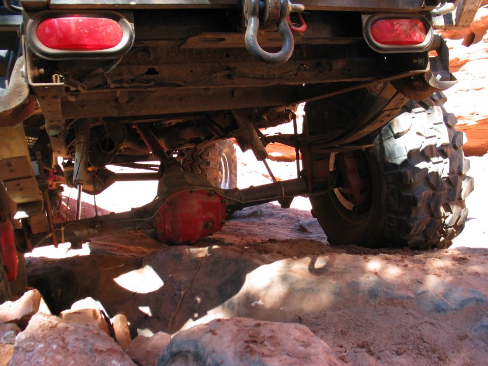 Underside of lifted truck on red rock showing red rear axle, leaf springs and shackle