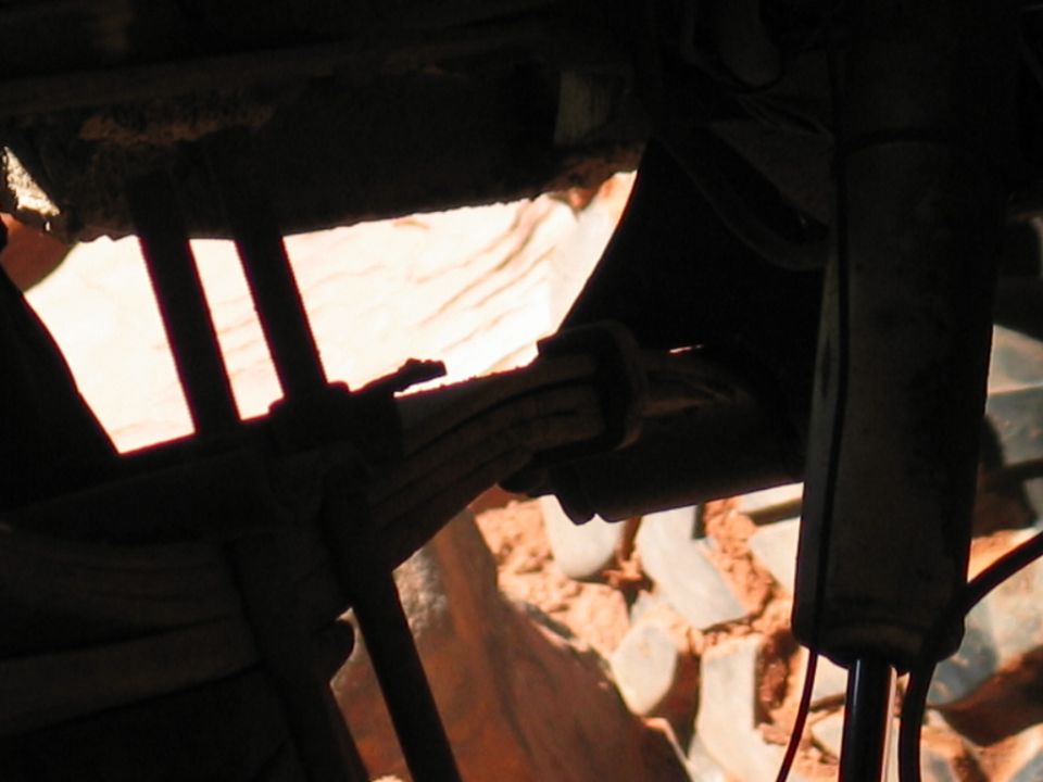 Backlit close-up of leaf spring, U-bolts and shock under a 4x4 on red rock