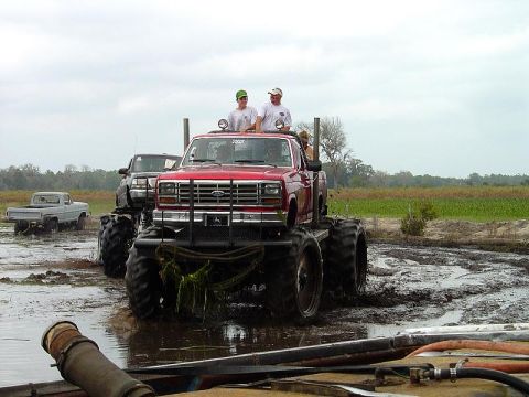 1993 Ford Bronco - Several trucks are in a muddy field, with one red Ford pickup modified for off-road use.