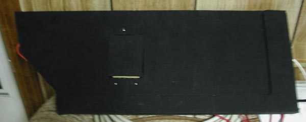 Black car stereo component with red wire, mounted on a patterned surface