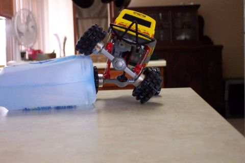1992 Ford Bronco - A yellow toy monster truck is shown on a table, with one of its large tires resting on a blue plastic bottle.