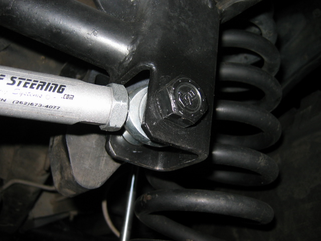 Steering linkage bolt attached to bracket near a coil spring underneath a vehicle