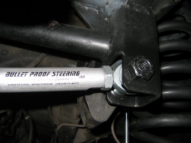 Silver Bullet Proof Steering component bolted to black knuckle near coil spring