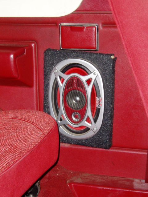 1990 Ford Bronco - A silver-and-red 6x9 coaxial speaker mounted in a black carpeted custom pod on the red rear side panel of a truck interior, just behind the…
