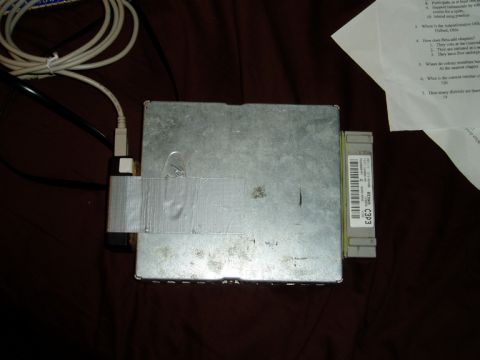 1990 Ford Bronco - A pulled engine control module lies face-up on dark cloth, its bare metal case patched with duct tape and a plug-in tuner module attached a…