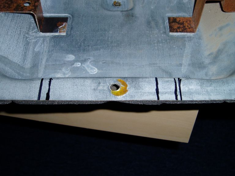 Metal bracket with black marker lines and a yellow-painted hole