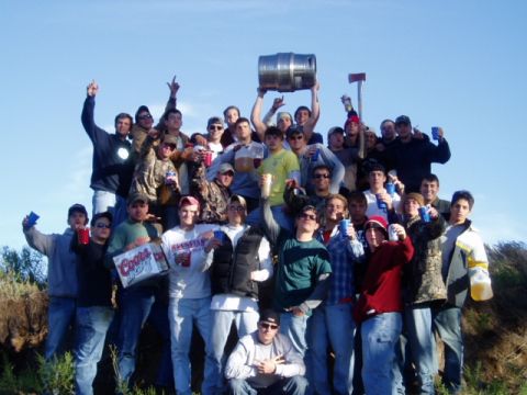 1990 Ford Bronco - A large group of people are gathered outdoors, holding drinks and a keg, under a clear blue sky.