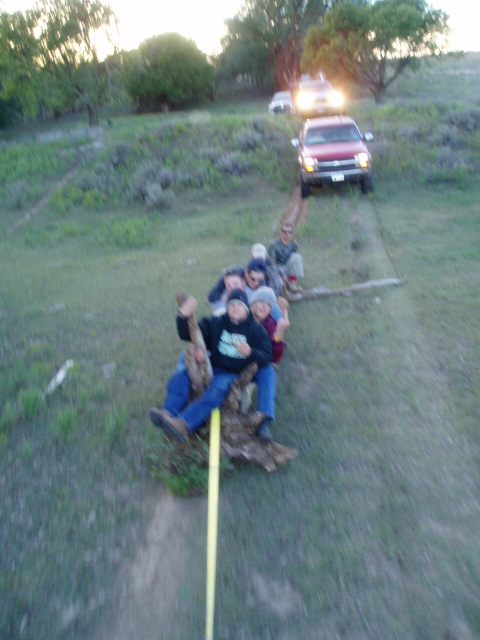 1990 Ford Bronco - A red SUV tows a log with several people riding on it down a grassy incline.