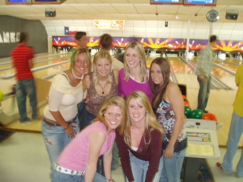 1990 Ford Bronco - A group of seven young women posing together for a photo at a bowling alley, with lit lanes, pins, and racks of colorful bowling balls visi…