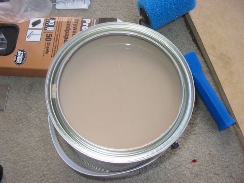 1988 Ford Bronco - Painting supplies are laid out on a carpeted floor, including a can of paint, a roller, and sandpaper.