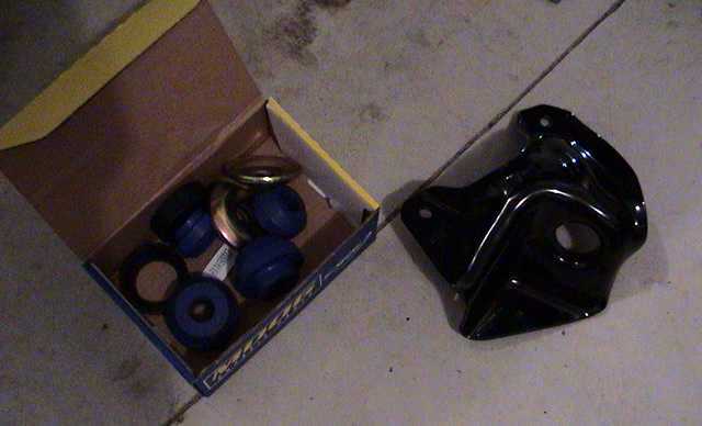 Blue polyurethane bushing kit in box beside black steel mounting bracket on concrete floor