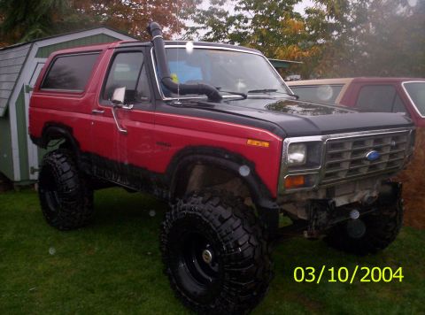 1983 Ford Bronco - Modified Ford Bronco with snorkel and off-road tires sits on grass near a shed, with another vehicle visible behind it.