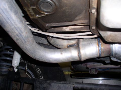 1990 Ford Bronco - Close-up view of the underside of a vehicle, focusing on the exhaust system and suspension parts.