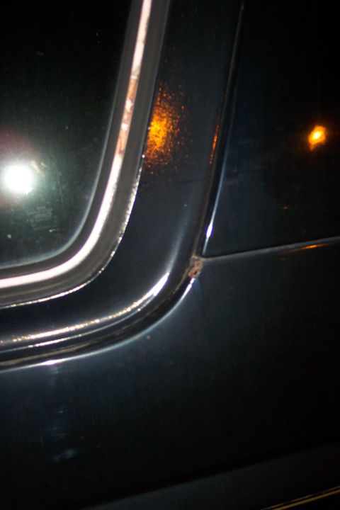 1986 Ford Bronco - Close-up view of a dark vehicle's body panel and window trim, showing a small rust spot.