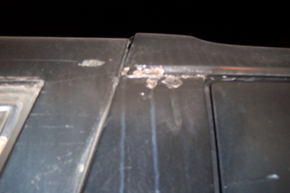 Chipped paint and bubbling rust at the top edge of a dark body panel, with rust streak