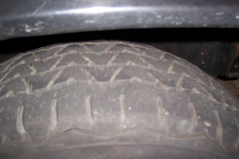 Close-up of dusty all-terrain tire tread under a dark fender lip at night