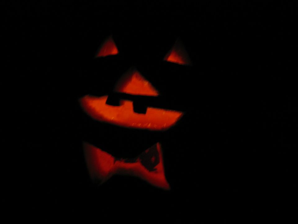 Carved pumpkin with triangular eyes, square nose, and a bow tie, illuminated from within