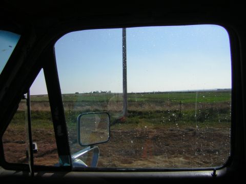 1995 Ford Bronco - View from inside a vehicle, looking out a side window at a rural landscape with fields and a distant farm under a clear blue sky.