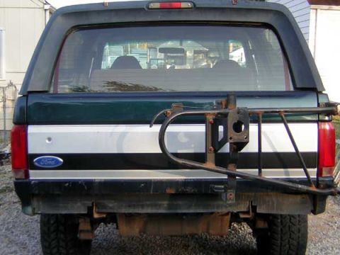 1995 Ford Bronco - The rear of a dark green and silver Ford Bronco is shown, a swing-away spare tire carrier.