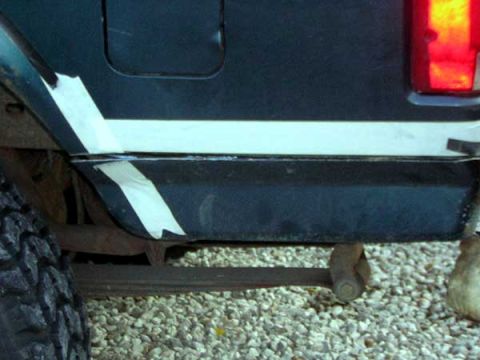 1995 Ford Bronco - Close-up of a dark SUV's rear quarter panel, showing tape applied to the fender and bumper area.
