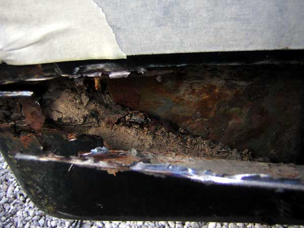 rusted out rocker panel on a vehicle, showing significant corrosion and debris