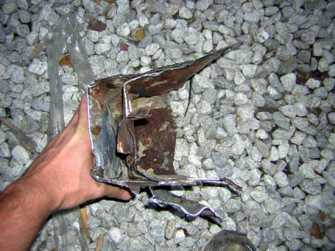 1995 Ford Bronco - Damaged metal part held by a hand against a background of gravel.
