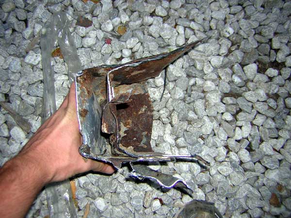 Hand holding a bent and rusted piece of metal, possibly a vehicle bumper fragment