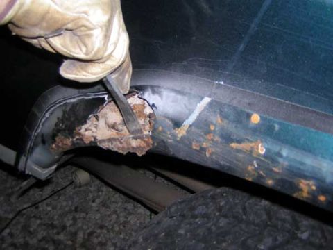 1995 Ford Bronco - A gloved hand uses a chisel to scrape away severe rust from a vehicle's fender area.