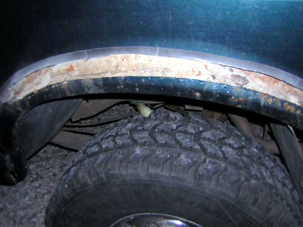 Black tube fender flare welded to a rusty cut wheel arch above a mud-terrain tire