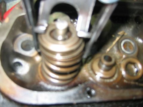 1992 Ford Bronco - Close-up macro of an engine valve spring being compressed by a spring compressor tool, showing the coiled spring, retainer, and valve keepe…