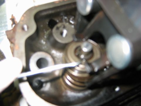 1992 Ford Bronco - Close-up of an engine cylinder head component showing a valve spring, retainer and rocker arm area, with a metal probe or tool touching the…